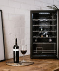 Cantinetta vini da 24 bottiglie 70 litri con porta aperta in ambiente rustico con muro in mattoni, bottiglia e calice di vino rosso