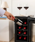 Persona che preleva bottiglia di vino da cantinetta da 8 bottiglie 25 litri in ambiente domestico elegante con calici